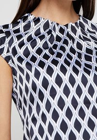 Blusa sin mangas de satén en azul marino con un patrón de olas en blanco, con cuello fruncido y textura suave.