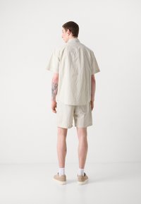 Striped short-sleeve shirt and matching shorts in light beige, made of a textured fabric with vertical stripes and a relaxed fit.