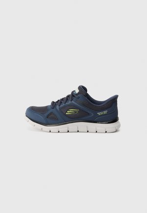 Navy blue Skechers slip-on sneaker with lightweight white sole and lime green logo on side, viewed from the outer side.