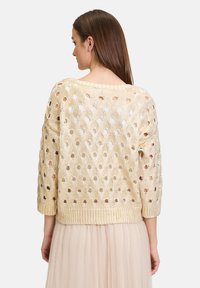 Strickpullover in Gold mit großen offenen Löchern, 3/4-Ärmeln und einem gerippten Saum. Weiche Textur und leichtes Design, das sich gut zum Schichten eignet.