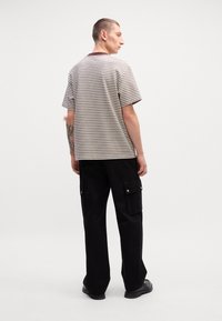 Pasiasta koszulka z krótkim rękawem w kolorze beżowym i brązowym, zestawiona z czarnymi spodniami cargo z kieszeniami bocznymi i srebrnymi akcentami.