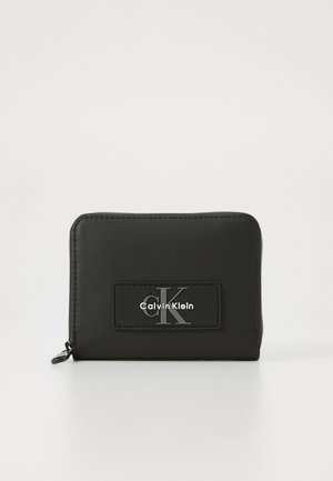 Portefeuille zippé noir en matériau lisse avec un patch noir surélevé portant le logo "Calvin Klein" et un accent argenté "cK".