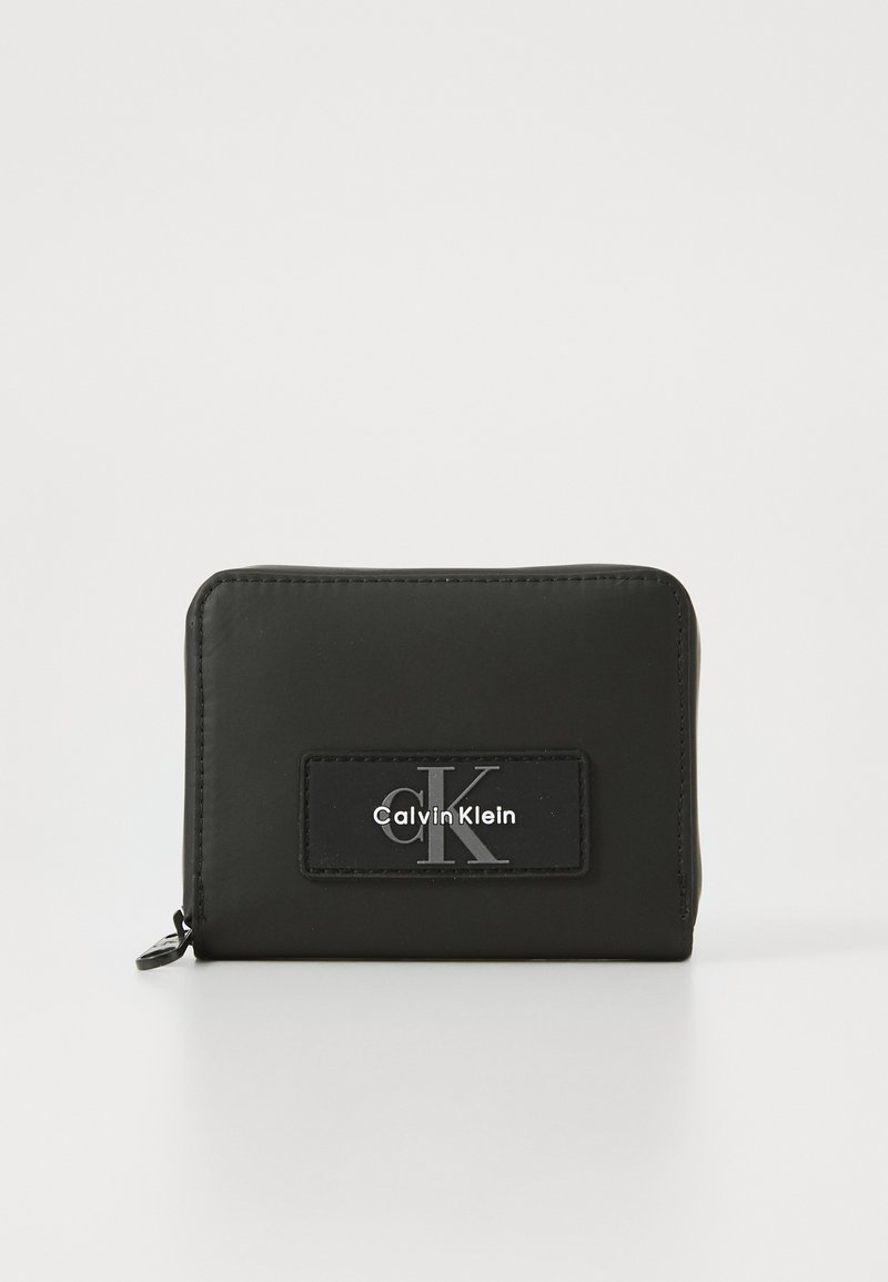 Zwarte portefeuille met rits, gemaakt van glad materiaal, met een verhoogd zwart patch met het "Calvin Klein" logo en een zilveren "cK" accent.