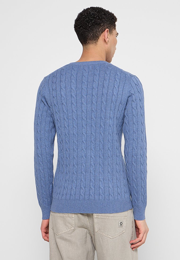 Jersey de punto azul con mangas largas, puños y dobladillo de canalé, que presenta un patrón texturizado y cuello redondo. Vista desde la parte posterior.