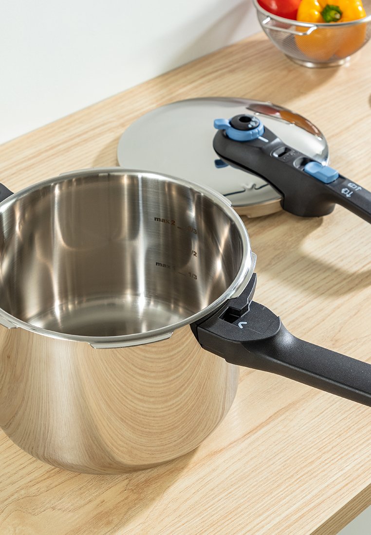 Autocuiseur en acier inoxydable avec une poignée et un couvercle en plastique noir. Les marquages intérieurs indiquent les niveaux de remplissage maximum. Surface lisse et réfléchissante.