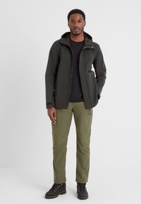 Black waterproof jacket with a hood, green cargo pants, and black boots. The jacket features a zipper and snap fasteners.