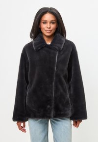 Jachetă neagră din blană artificială cu guler, croi oversized și buzunare laterale. Textură moale și un design curat, minimalist.
