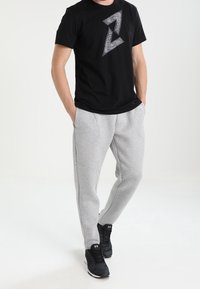 Svart t-shirt med korta ärmar och vit geometrisk mönstring; grå sweatpants med en smal design; svarta sportskor.