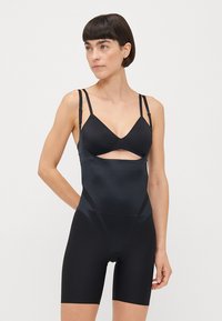 Black bodysuit with adjustable straps, featuring a bra design and mid-thigh length. Smooth texture and seamless construction.