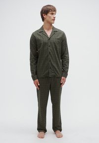 Conjunto de pijama de cuadros verdes que incluye una camisa abotonada con cuello en punta y pantalones a juego con cintura elástica. Textura suave.