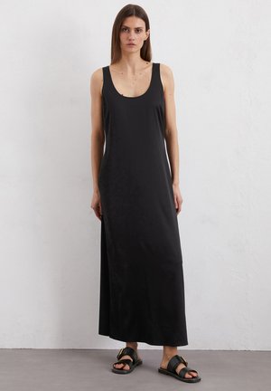 Abito maxi nero con scollatura a cuore e spalline larghe, realizzato in tessuto morbido. Abbinato a sandali neri piatti con dettaglio fibbia metallica.
