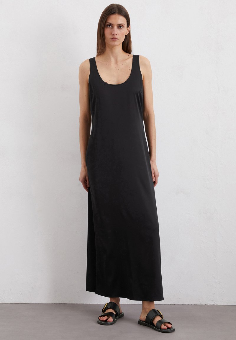 Robe maxi noire avec un col en scoop et des bretelles larges, fabriquée en tissu lisse. Associée à des sandales noires plates avec un détail de boucle métallique.