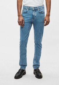 Svetlomodré riflové nohavice s priamym strihom, piatimi vreckami a jemne vyblednuté. Nosia sa s čiernymi slip-on topánkami s textúrovanou podrážkou.