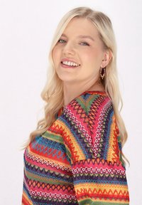 Mehrfarbige Bluse mit geometrischen Mustern in Rot, Grün, Blau und Gelb. Der Stoff hat eine strukturierte Strickoptik und lange Ärmel.
