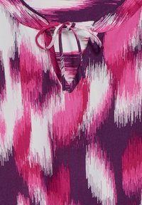 Blusa viola con un motivo astratto rosa, dotata di un nodo al collo, tessuto morbido e maniche corte.