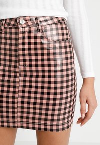 Różowa i czarna mini spódniczka w kratkę o błyszczącym wykończeniu, z przodem zapinanym na guziki, detalami z kieszeniami oraz kontrastującym przeszyciem.