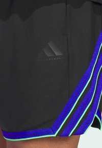 Pantalones cortos deportivos negros con un acabado texturizado, que presentan acentos de rayas moradas y azul claro, y un discreto logo de adidas en negro.
