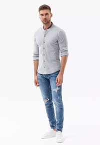 Grijze langarmpoloshirt met een smalle kraag. Lichtblauwe versleten jeans met scheuren. Witte sneakers maken de outfit compleet.