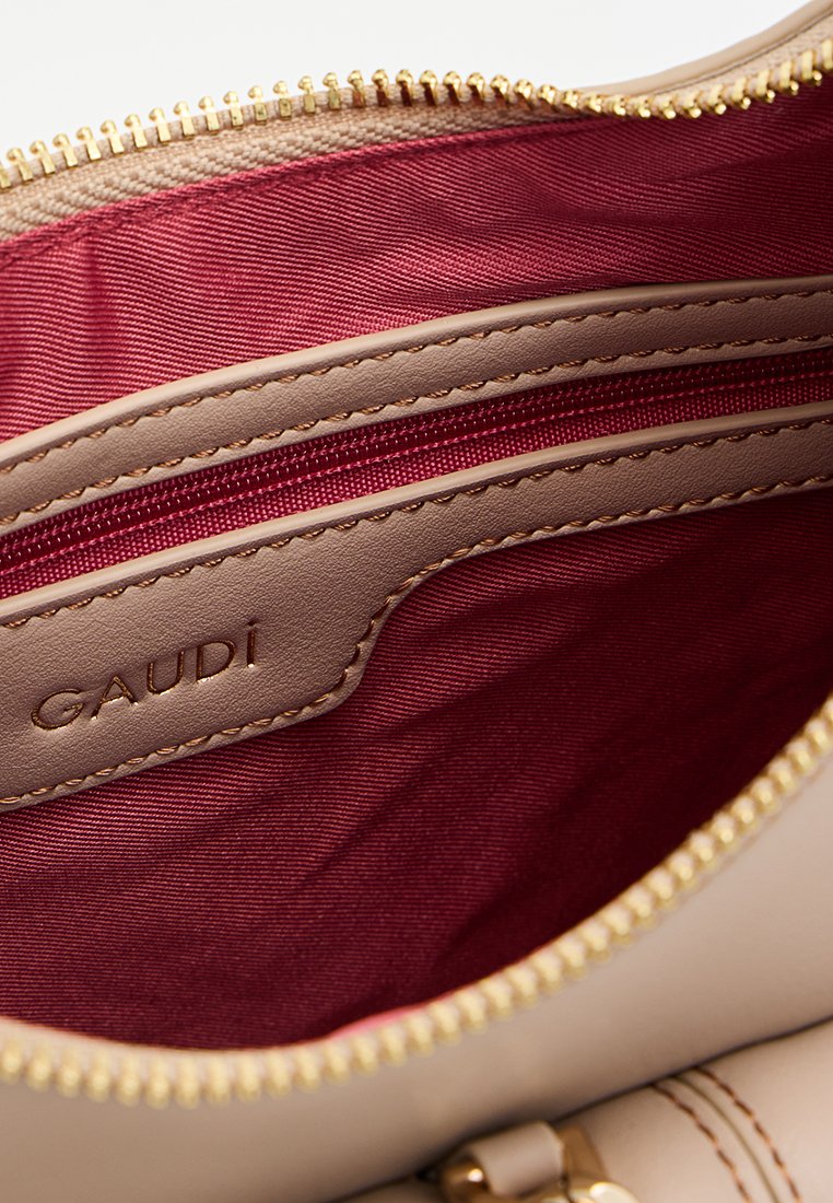 Interno di una borsa in pelle beige con fodera in tessuto bordeaux, tasca con zip e etichetta in pelle "GAUDI" impresso vicino alla zip.