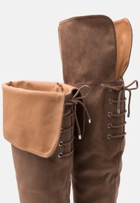 Brązowe buty za kolano z miękkiego zamszu, z brązowym skórzanym mankietem, sznurowanym przodem i srebrnymi oczkami.