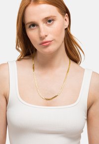 Collana a catena color oro con anelli intrecciati e finitura lucida, appoggiata su una canotta bianca a righe. Design semplice, spessore medio.