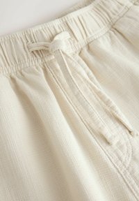 Zbliżenie na teksturowany kremowy materiał spodni w talii z elastyczną gumką i zawiązanym sznurkiem.