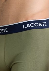 Olijfgroene boxershort met een marineblauwe elastische tailleband waarop het "LACOSTE"-logo in het wit is afgebeeld. Soepele textuur, aansluitend ontwerp.