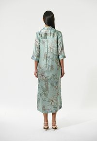 Langes, mintgrünes Kleid mit Blumenmustern, Dreiviertelärmeln und einer lockeren Silhouette. Weicher Stoff mit glatter Textur.