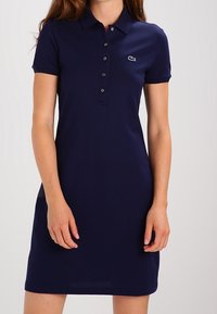 Navy polo dress made of cotton, featuring a collared neckline, button placket, and a small embroidered logo on the left chest.