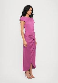 Rochie fucsia cu un design drapat, mâneci scurte și o f slit lateral. Confecționată dintr-un material neted, asortată cu sandale cu toc și curea la gleznă de culoare bej.
