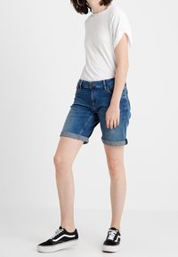 Blå jeansshorts med uppvikta muddar, bära tillsammans med en vit t-shirt och svarta låga sneakers. Enkel design, standardpassform, inga synliga mönster.