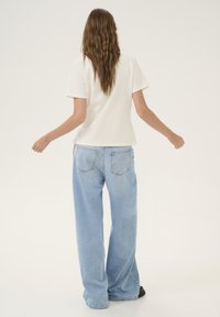 Top bianco a maniche corte abbinato a jeans a gamba larga blu chiaro. I jeans presentano due tasche posteriori e una texture leggermente sbiadita.