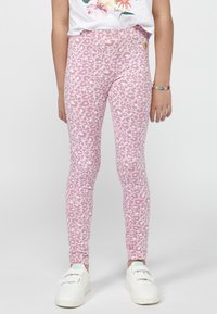 Leggings roses avec un motif léopard, fabriqués dans un matériau extensible, présentent un design ajusté et sont associés à des baskets blanches.