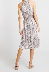 Maxi dress in a light pink fabric with a black snake print pattern. Features a halter neck and an elastic waist, flowing to mid-calf length.