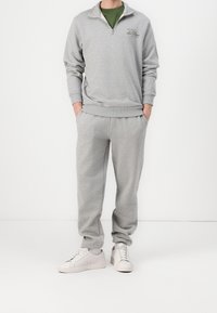 Sweat-shirt gris clair à fermeture éclair avec poignets côtelés et petit logo. Assorti à un pantalon de jogging gris et des baskets blanches. Tenue décontractée sportive.