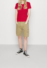 Rød bomulds t-shirt parret med beige cargo shorts med sidelommer, båret med sorte høje sneakers. Enkel, afslappet påklædning.