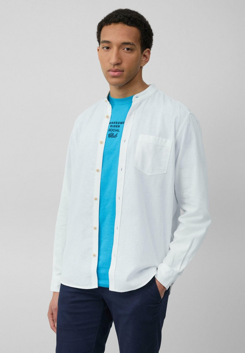 Witte button-up shirt met een zachte textuur, voorzien van een zak, gedragen over een felblauw t-shirt met zwarte tekst. Geen zichtbare patronen.