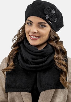 Beret negro de punto con acentos decorativos de rosa y una bufanda negra a juego. Textura suave con un diseño drapeado y en capas.