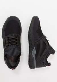 Scarpe sportive nere con superiore in mesh testurizzato, dettagli a strisce in contrasto, chiusura con lacci e una suola in gomma spessa.