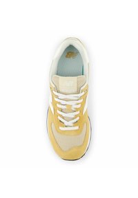 Beige och gul sneaker med mesh- och mockamaterial, vita snören och New Balance-logotyp på tungan. Inredningen har ett lätt blått foder.