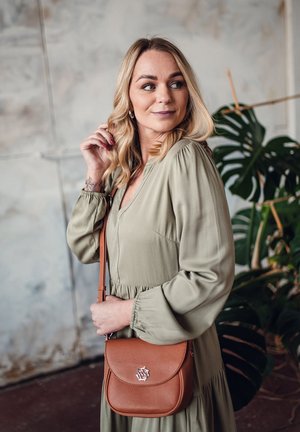 Olive green dress with puff sleeves and a fitted bodice, paired with a brown crossbody bag featuring a floral accent. Indoor setting.