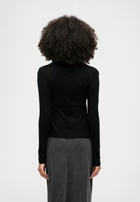 Črn dolg rokav majica z oprijetim krojem in okroglo ovratnikom, v kombinaciji s temno sivo, teksturirano krilo; gladek material, minimalistični videz.