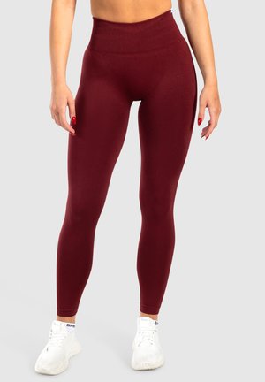 Leggings bordeaux a vita alta con una texture liscia, una forma aderente e una cintura larga, abbinati a scarpe da ginnastica bianche.