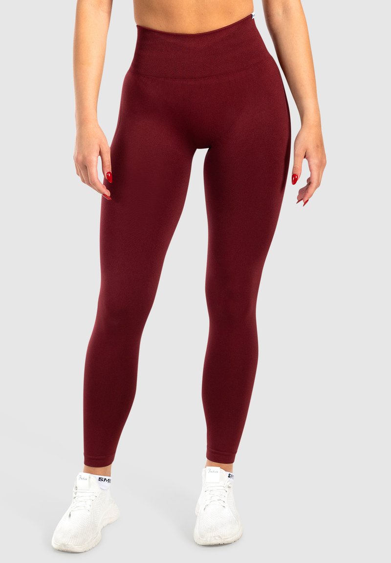Bordeaux hoge taille legging met een gladde textuur, aansluitende pasvorm en brede tailleband, gecombineerd met witte sportschoenen.