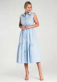 Jasnoniebieska, bezrękawnikowa sukienka zapinana na guziki z falbaniastą spódnicą i detalem w postaci paska w talii. Wykonana z gładkiego materiału, do kolan, o luźnym kroju.