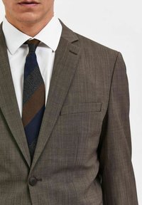Bruine, gestructureerde colbert met één knoop, notch-lapels en een borstzak. Gecombineerd met een witte overhemd en een gestreepte stropdas.