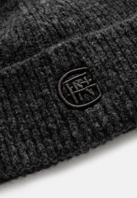 Zwarte gebreide beanie met een gestructureerd patroon en een geborduurd logo aan de donkere kant, waarmee het zachte materiaal wordt benadrukt.