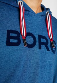 Felpa con cappuccio blu con una finitura testurizzata, caratterizzata da un grande logo "BORG" blu scuro e stringhe di regolazione a strisce rosse, bianche e nere.