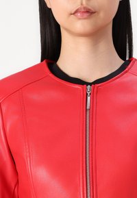 Rote Lederjacke mit rundem Ausschnitt und silbernem Reißverschluss. Die Textur ist glatt mit auffälligen Nähten entlang der Nähte.