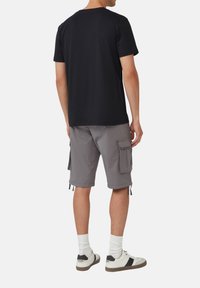 Czarna koszulka krótki rękaw, szare szorty cargo z bocznymi kieszeniami, białe skarpetki i beżowe sneakersy z czarnymi akcentami. Gładkie tło.